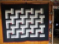Full view of quilt hanging showing geometric interlocking l-shape pattern in black, white, gray, and red.