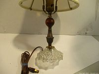 Front view of the lamp showing textured glass base, wood sphere, metal detailing, and beige lampshade.