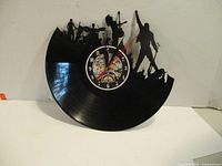 Side view of the vinyl record clock showing the detailed cutout silhouettes of the rock band and fans, and the clock face with visible gears.