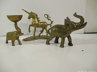 Three solid brass figures: an elephant with raised trunk, a unicorn on a decorative base, and an elephant-shaped candle holder with perforated bowl.