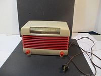 Front view of vintage Airline radio showing cream casing, red front grille, two control knobs, and power cord with plug.