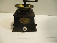 Front view of vintage cast iron coffee grinder with brass bowl, hand crank, and decorative brass plate on the front.