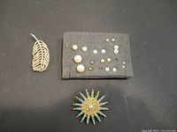 Overview of entire jewelry set with leaf brooch, sunburst brooch, and stud earrings on black background