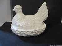 White glazed ceramic covered dish shaped as a hen on nest, side view.