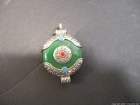 Front side of vintage Tibetan pendant showing green stone, silver metal accents, and red and blue enamel dots.
