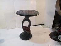 Front angle view of the round wooden table / plant stand showing top and base with carved artistic design.