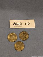 Three US dollar coins arranged in a triangular layout on gray fabric. Coins are gold-colored showing detailed portraits.