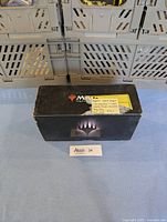 Closed black Magic the Gathering branded card box with a handwritten sticky note describing set contents and value