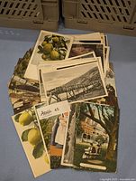 Stack of postcards showing various subjects including lemon fruit still life, a black and white bridge scene, and a garden setting with a woman seated in front of a building.