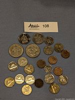 21 Canadian coins laid out on grey fabric background including coins with Canadian coat of arms, floral symbols, and various metal types and sizes.