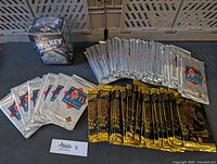 Lot of sealed hockey card packs arranged on a table with one sealed full box upright in the corner. Visible are silver and black/gold sealed packs from different series.