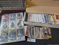 Photo showing a binder of protected baseball cards alongside a box full of loose cards, mainly modern MLB cards.