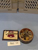 Photo showing vintage Nippyclip tie clip in original box and round tin filled with assorted men's cufflinks and tie pin chains.