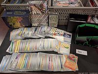 Over 400 bulk Pokemon cards spread on table with a jumbo Ursaluna promo card, sealed Magneton promo visible, mini binders and card organizer box.