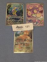 Photo of Bruxish, Exeggcute, and additional Pawmot Pokemon cards laid flat showing the full artwork and text details with a tag labeled 'Atomic Collectibles 131'.