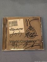 Front cover of the CD case with signatures on brown cardboard-style background and barcode sticker.