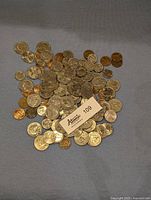 Pile of mixed US coins including pennies, nickels, dimes, and quarters on blue cloth background with auction tag visible.