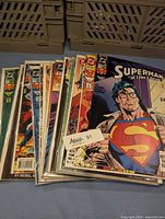 Stack of 16 vintage Superman comic books in plastic sleeves, showing a variety of cover art featuring Superman.