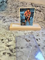 Front of vintage 1961-62 AB McDonald Topps hockey card held upright in a wooden holder with clear plastic sleeve nearby.