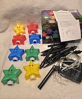 Colorful star-shaped solar lights, eight pieces, laid out on a surface including yellow, red, blue, and green stars. Black stakes and instruction sheet visible.