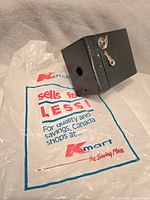 Photo of the Brownie camera showing the front and side with wind key next to a plastic shopping bag.