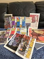 Front view of assorted Comic Shop News magazines arranged on a couch showing colorful comic character covers