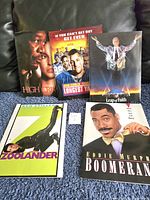 Five assorted movie press release kits displayed upright on a couch, showing covers for High Crime, The Longest Yard, Leap of Faith, Zoolander, and Boomerang.