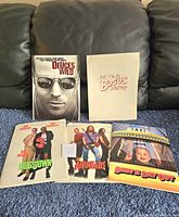 Assorted vintage movie press folders and promotional materials for films including Deuces Wild, Bogus Journey, Doggstown, Airheads, and Baby's Day Out, displayed on a dark couch.