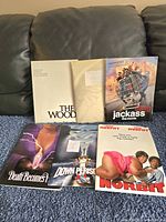 Photo showing multiple movie press release folders arranged on couch, including The Woods, Jackass the Movie, Death Becomes Her, Down Periscope, and Norbit.