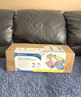 Photo of the boxed sealed Duck Covers outdoor rectangle seat cushion, placed on denim surface, showing brand and product details.