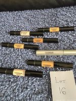 Six Covergirl makeup items on blue textured fabric background, five concealers and one mascara tube. Paper note with 'Lot 16' handwritten shown.