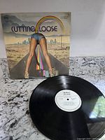 Photo of Cutting Loose vinyl record with cover showing person in denim shorts with rainbow on road.