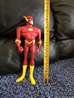 The Flash action figure standing upright next to a ruler showing height approximately 10 inches.