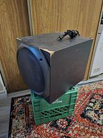 Side angle view of Logitech Z-5500 subwoofer showing the speaker grille and damaged corner of enclosure with power cord on top.