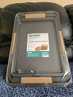 Three black nonstick cookie sheets stacked and shrink-wrapped with a label showing the brand InStyle and product details.