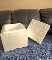 White Styrofoam cooler open with lid placed beside, placed on dark surface with sofa background