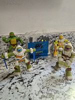 Four Teenage Mutant Ninja Turtle figures on a granite countertop, showing color, pose, and accessories.
