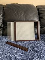 Photo showing the Umbra picture frame with multiple clear sliding glass panels separated, lying on a blue carpet in front of a dark leather couch.
