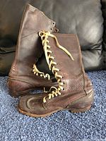 Side profile view of both vintage brown leather boots placed on a carpet showing high ankle design and cream laces.