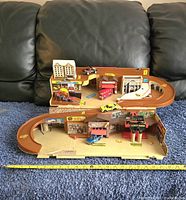 Overview of the full playset showing the multi-level orange track with several die-cast cars placed on the ramps and parking areas, and city buildings including fire station and police station.