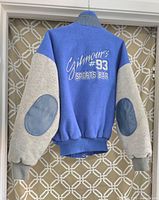 Blue and grey men's jacket with elbow patches and embroidered logo on back.