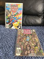 Two Justice League comic books placed separately showing front cover art with superheroes and crowd of characters.