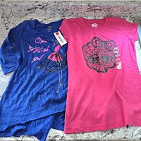 Two girls tops laid flat, one blue with long sleeves and 'One Stylish Girl' text, one pink with lace rose design.