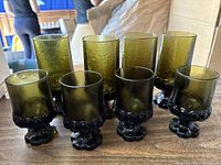 Twelve vintage green goblet glasses arranged in two rows: smaller 5-inch glasses in front and taller 7-inch glasses behind.