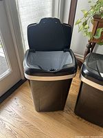 Front view of one Hefty brand black and silver trash bin with the swing lid open showing the interior