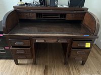 Front view of the antique wooden roll-top desk showing seven drawers and the roll-top part with the glass top surface visible.