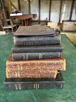Stack of 8 books including 3 vintage Bibles, 4 antique Bibles, and 1 hymnal book stacked on a table showing covers and spines with wear and damage.