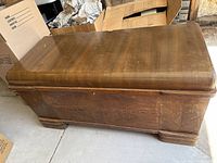 Angled view showing the exterior of the rectangular solid wood cedar chest with natural finish and decorative inlay on the front panel.