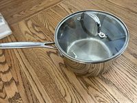 Stainless steel saucepan with glass lid and long handle on wooden floor