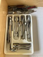 Cutlery tray with organized knives, forks, spoons, and additional serving utensils including a pair of kitchen scissors and tongs